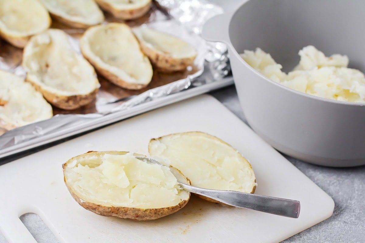 Easy twice baked potatoes are loaded with sour cream, cheese, bacon, and seasonings for the perfect savory side or main dish! Spooning out the center of a cooked baked potato into a mixing bowl.