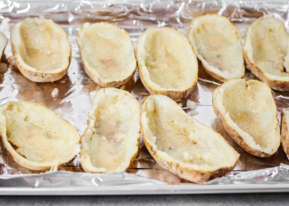 Easy twice baked potatoes are loaded with sour cream, cheese, bacon, and seasonings for the perfect savory side or main dish! Hollowed out baked potato halves on a baking sheet.