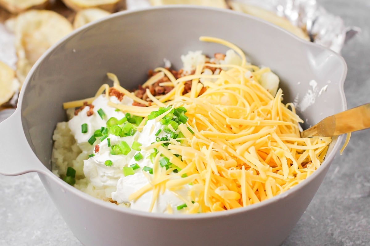 Easy twice baked potatoes are loaded with sour cream, cheese, bacon, and seasonings for the perfect savory side or main dish! Unmixed twice baked potato filling in a mixing bowl.