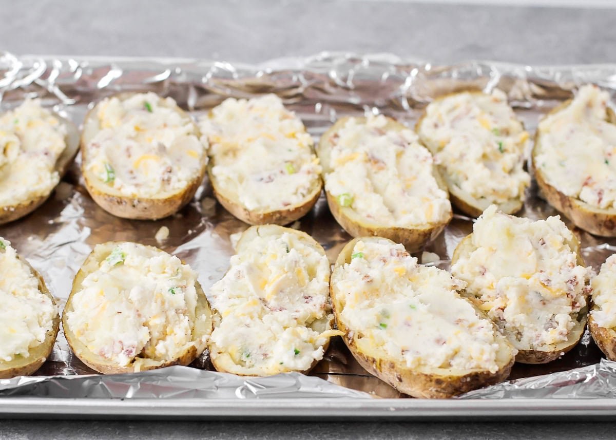 Easy twice baked potatoes are loaded with sour cream, cheese, bacon, and seasonings for the perfect savory side or main dish! Filling added to the baked potato halves on a baking sheet.