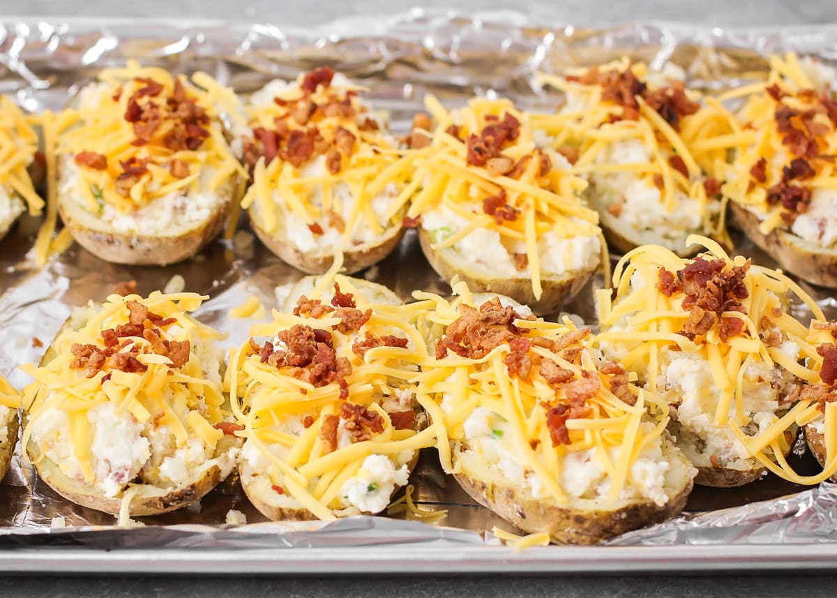 Easy twice baked potatoes are loaded with sour cream, cheese, bacon, and seasonings for the perfect savory side or main dish! Filled twice baked potato halves with shredded cheese and bacon crumbles on top on a baking sheet
