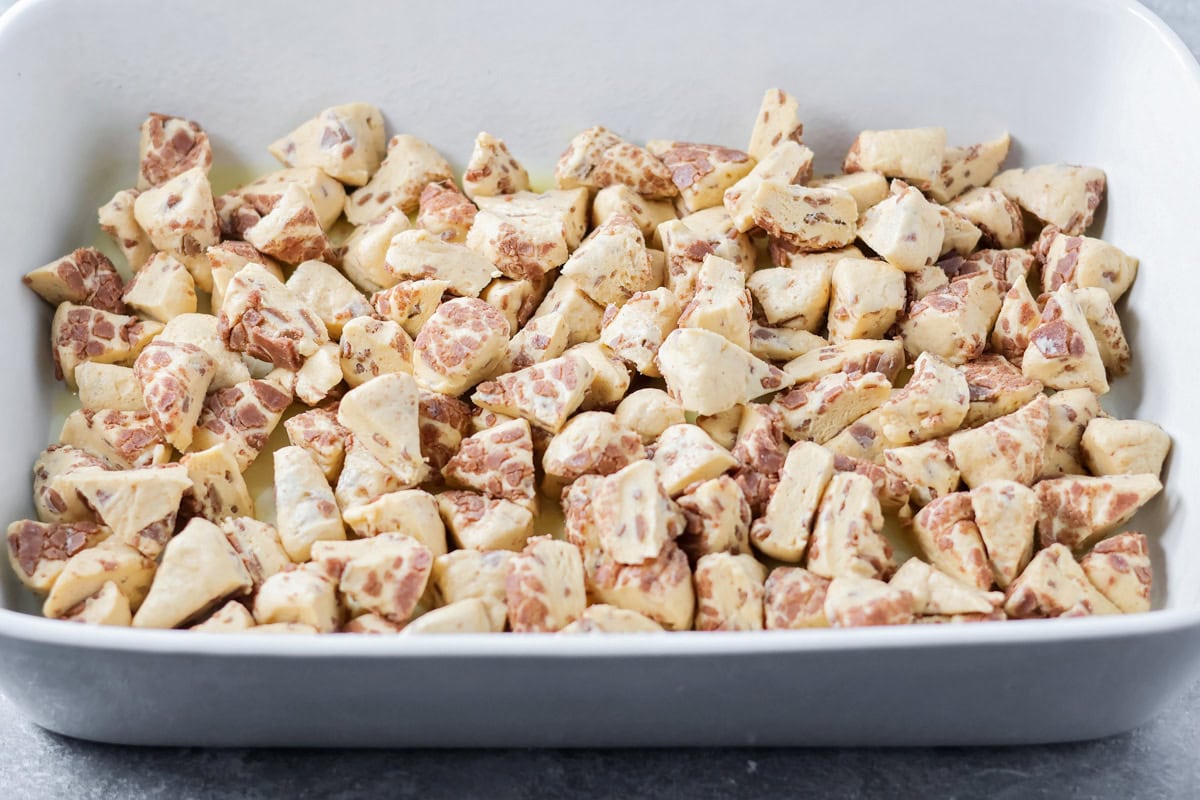 Warm, gooey, and easy to make, this cinnamon roll casserole turns refrigerated rolls into a cozy breakfast everyone will love. Cinnamon roll dough cubes spread at the bottom of a ceramic baking dish.