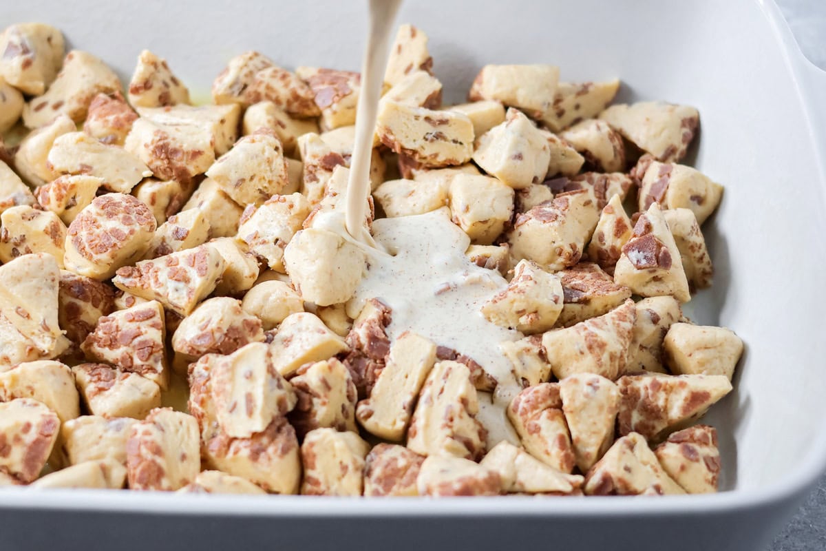 Warm, gooey, and easy to make, this cinnamon roll casserole turns refrigerated rolls into a cozy breakfast everyone will love. Pouring custard over cinnamon roll dough cubes.