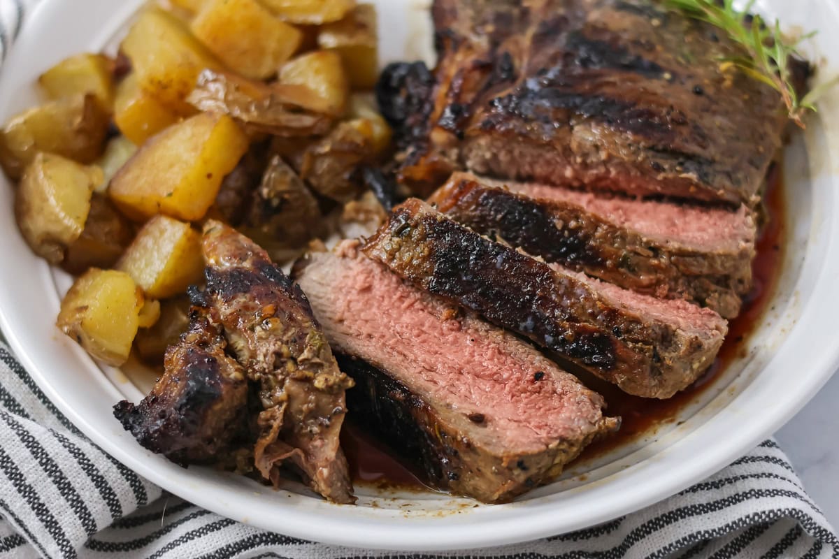 Sliced Italian rib eye on a white plate with diced roasted potatoes.
