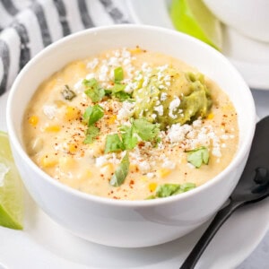 Mexican street corn soup served in a white bowl topped with cilantro and guacamole.