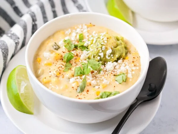 Mexican street corn soup served in a white bowl topped with cilantro and guacamole.