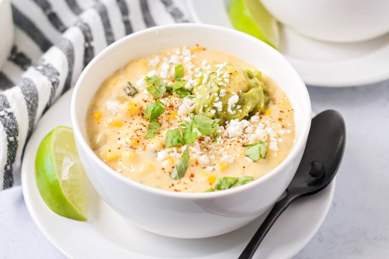 Mexican street corn soup served in a white bowl topped with cilantro and guacamole.