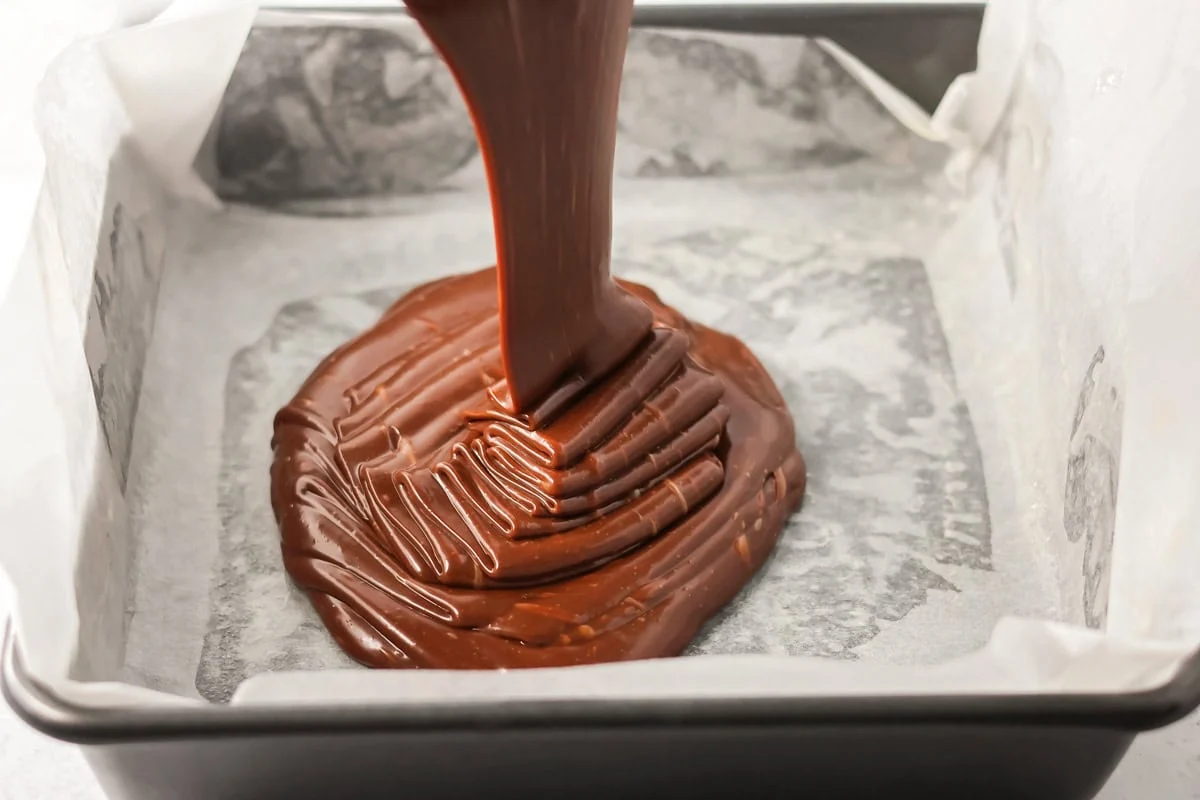 Pouring fudge batter in a parchment lined baking pan.