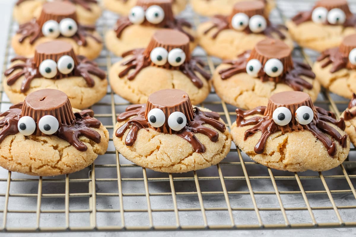These easy and cute Peanut Butter Spider Cookies are the perfect sweet treat to get you in the spooky spirit. A wire rack of peanut butter cookies with chocolate peanut butter cup spiders on top.