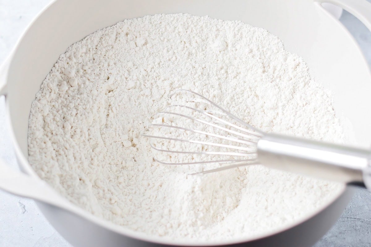 Mixing cake mix with pudding mix and spices in a white mixing bowl.