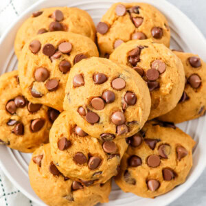 Pumpkin chocolate chip cookies stacked on top of each other on white plate.
