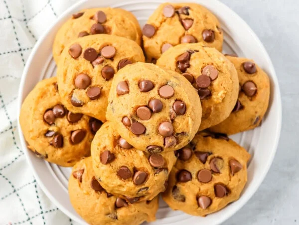 Pumpkin chocolate chip cookies stacked on top of each other on white plate.