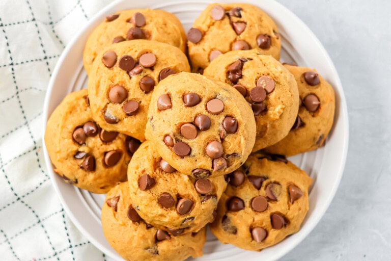 Pumpkin chocolate chip cookies stacked on top of each other on white plate.