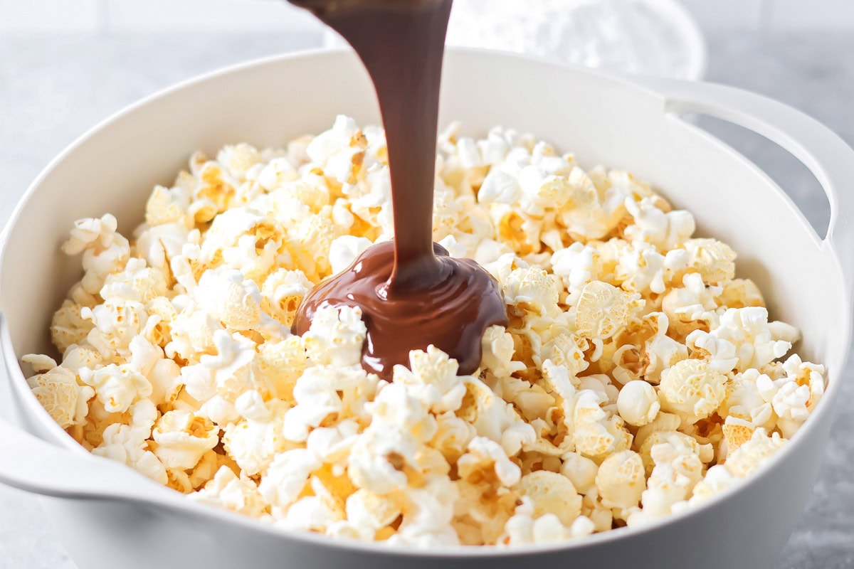 Puppy Chow Popcorn is an irresistible sweet and salty snack that's easy to make and guaranteed to be a hit. Pouring the chocolate peanut butter coating over a bowl of fluffy popcorn.
