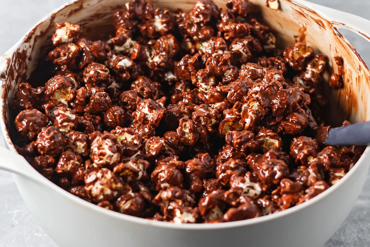 Puppy Chow Popcorn is an irresistible sweet and salty snack that's easy to make and guaranteed to be a hit. A bowl of popcorn coating in a chocolate peanut butter sauce.