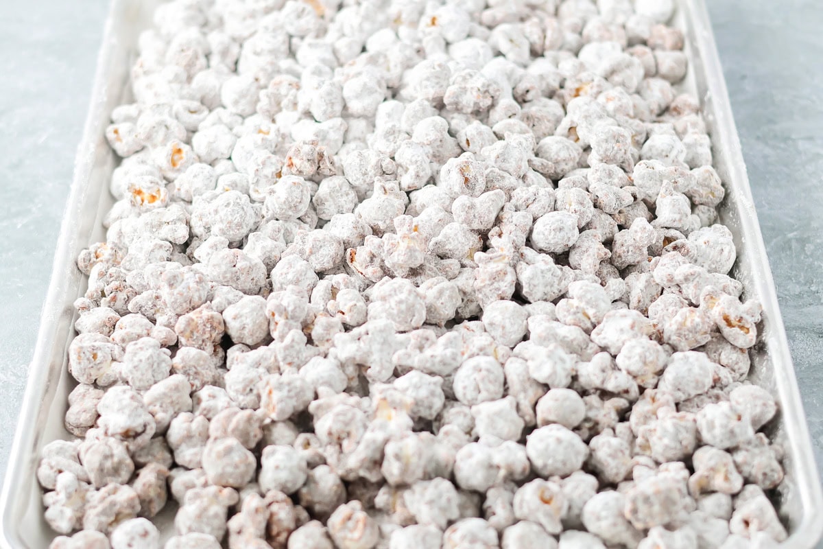 Puppy Chow Popcorn is an irresistible sweet and salty snack that's easy to make and guaranteed to be a hit. Coated puppy chow popcorn spread out to cool on a baking sheet.
