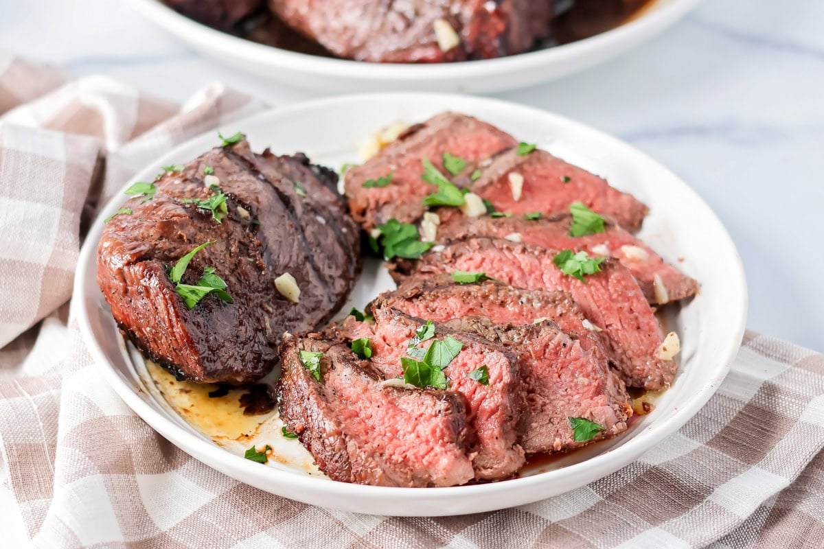 Two sirloin steaks on a dinner plate, one cut into slices to show the delicious center.