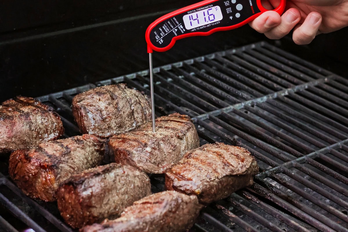 Using a meat thermometer to check the internal temperature of grilling steak.