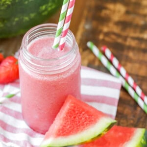 Watermelon smoothie recipe in a cup with straws and watermelon near it.