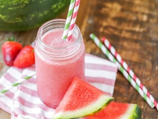 Watermelon smoothie recipe in a cup with straws and watermelon near it.