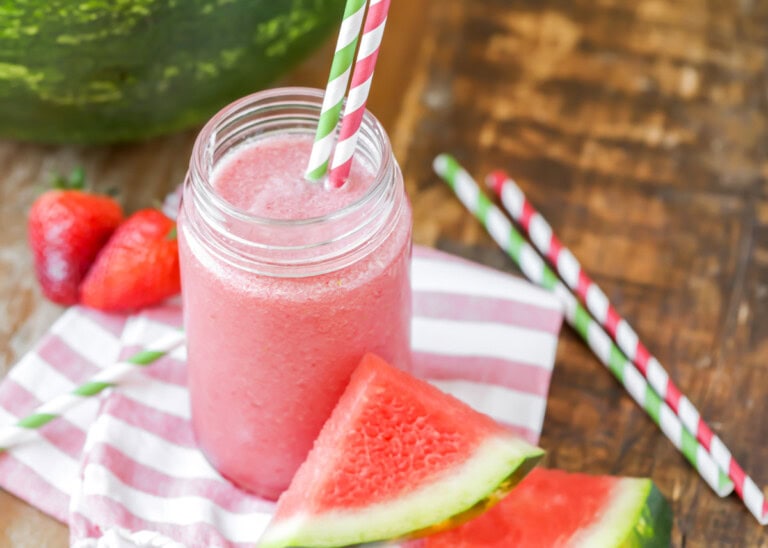 Watermelon smoothie recipe in a cup with straws and watermelon near it.