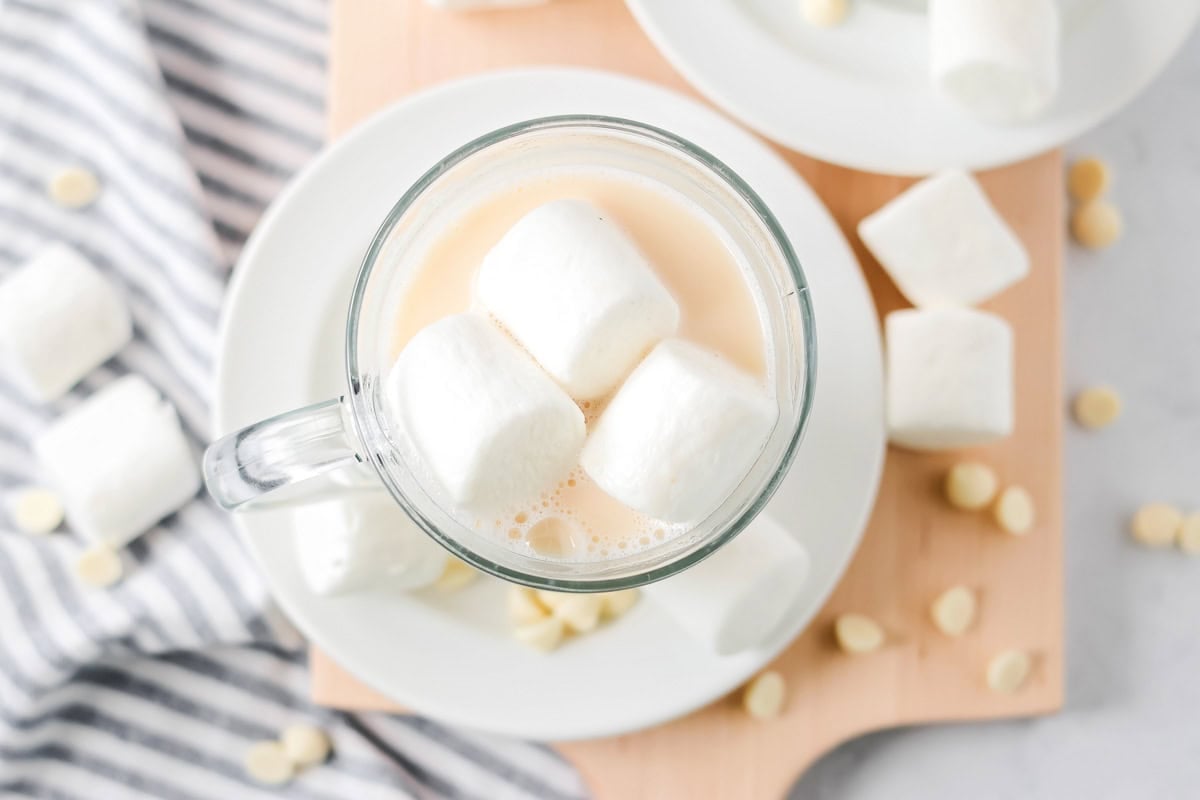 Decadent double chocolate hot chocolate is filled with white chocolate chips, chocolate milk, and heavy whipping cream for one rich cupful!! White Chocolate Hot Cocoa drink in glass mug with marshmallows in it.