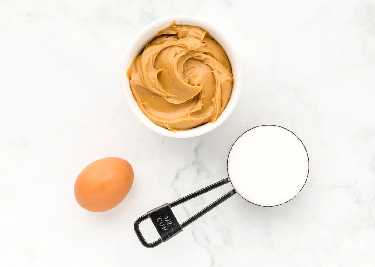 Delicious 3 ingredient peanut butter cookies take just minutes to throw together and are so easy the kids can make them! Ingredients to make 3 Ingredient peanut butter cookies on a kitchen counter.