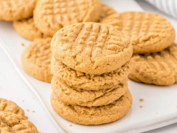 3 ingredient peanut butter cookies stacked on a cookie sheet.