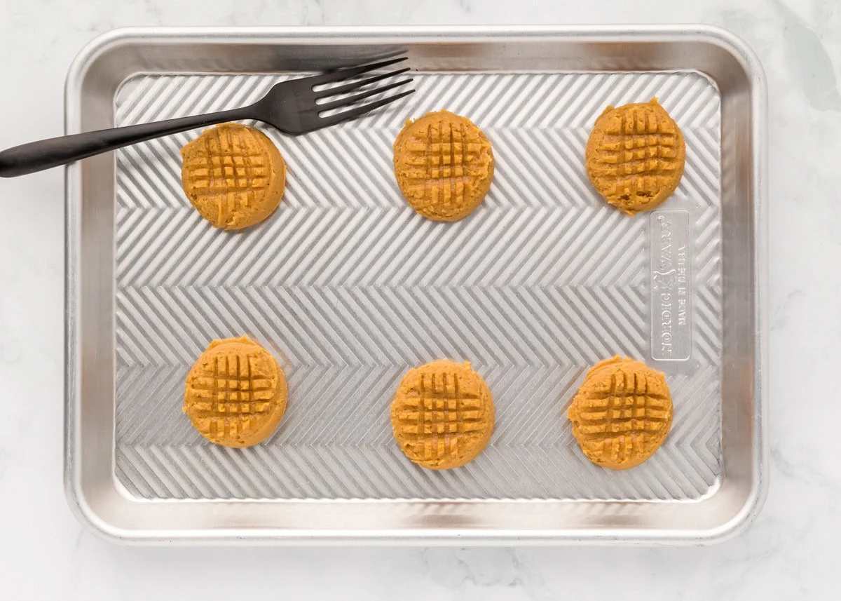 Delicious 3 ingredient peanut butter cookies take just minutes to throw together and are so easy the kids can make them! Cross crossed peanut butter cookie dough balls on a baking sheet.