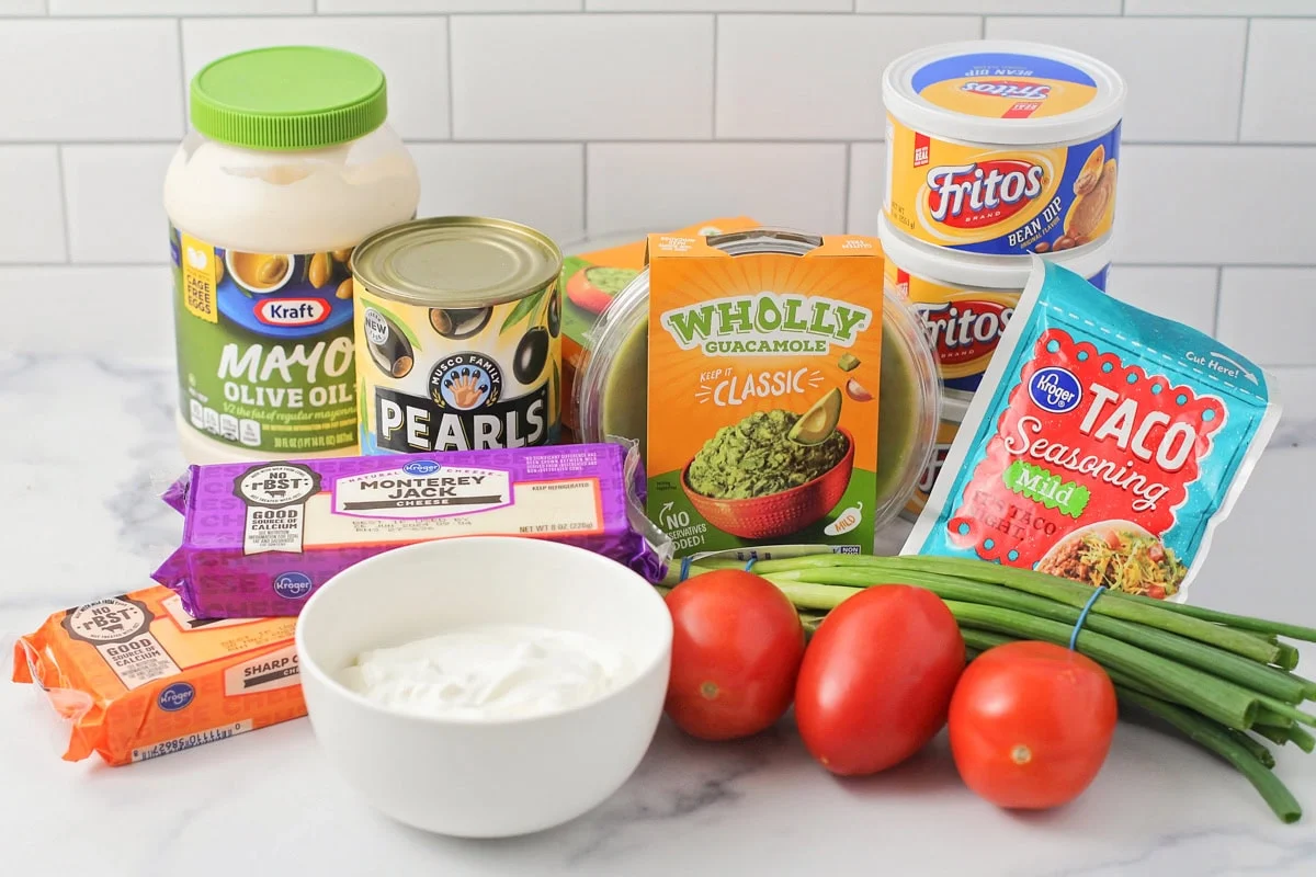 This 10-minute 7 layer bean dip is a must-have at every function! It has loads of flavor and all your favorite dip ingredients! Ingredients to make 7 layer bean dip on a kitchen counter.