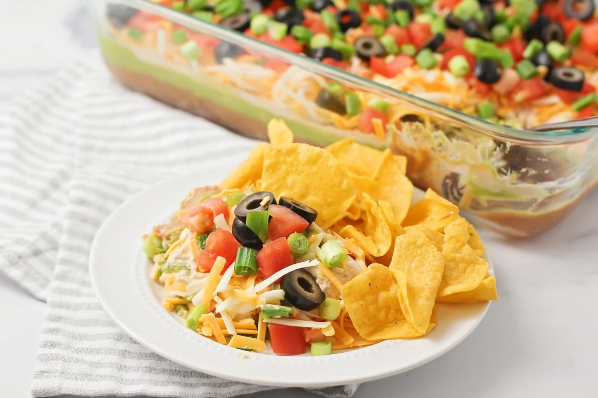 This 10-minute 7 layer bean dip is a must-have at every function! It has loads of flavor and all your favorite dip ingredients! A scoop of 7 layer bean dip on a serving plate along with tortilla chips.