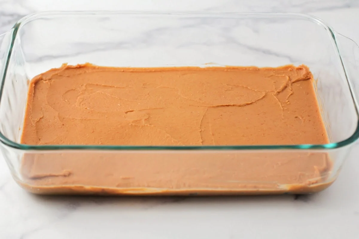 This 10-minute 7 layer bean dip is a must-have at every function! It has loads of flavor and all your favorite dip ingredients! A layer of Frito Lay bean dip spread in a glass baking dish.