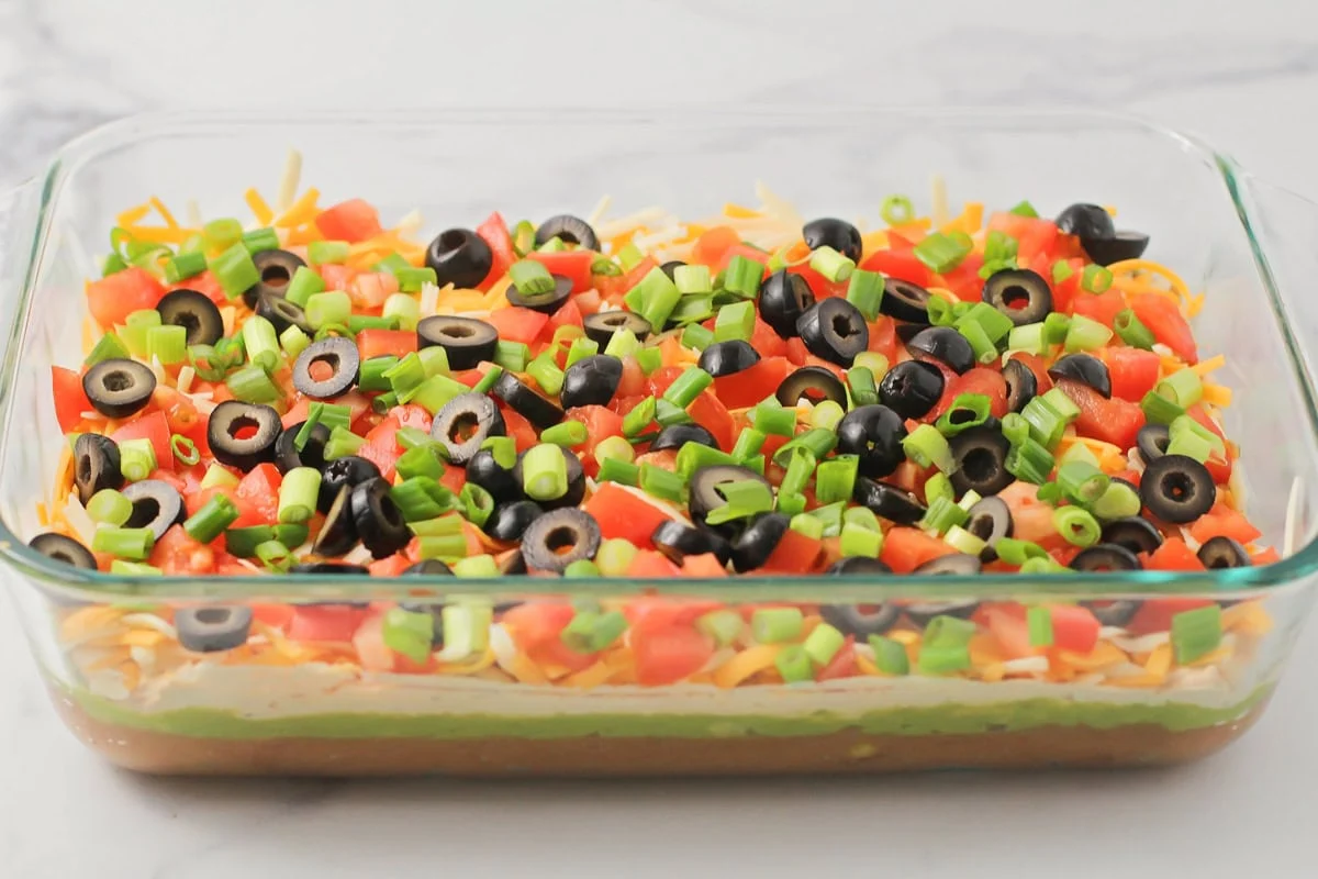 This 10-minute 7 layer bean dip is a must-have at every function! It has loads of flavor and all your favorite dip ingredients! A 7 layer bean dip topped with sliced olives and green onions.