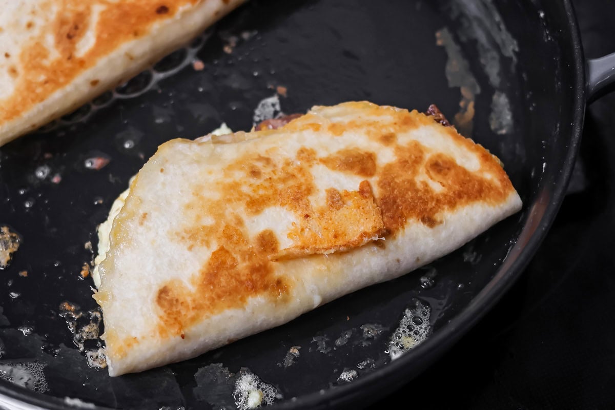 Crispy breakfast quesadillas packed with savory ingredients for a fast family meal that works for breakfast or dinner. Browning the quesadilla in a skillet.