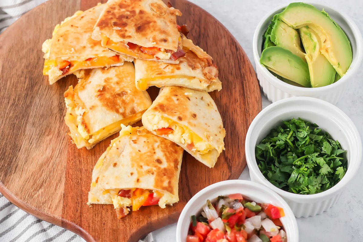 Crispy breakfast quesadillas packed with savory ingredients for a fast family meal that works for breakfast or dinner. Breakfast quesadillas cut in half and stacked on a wooden serving board.
