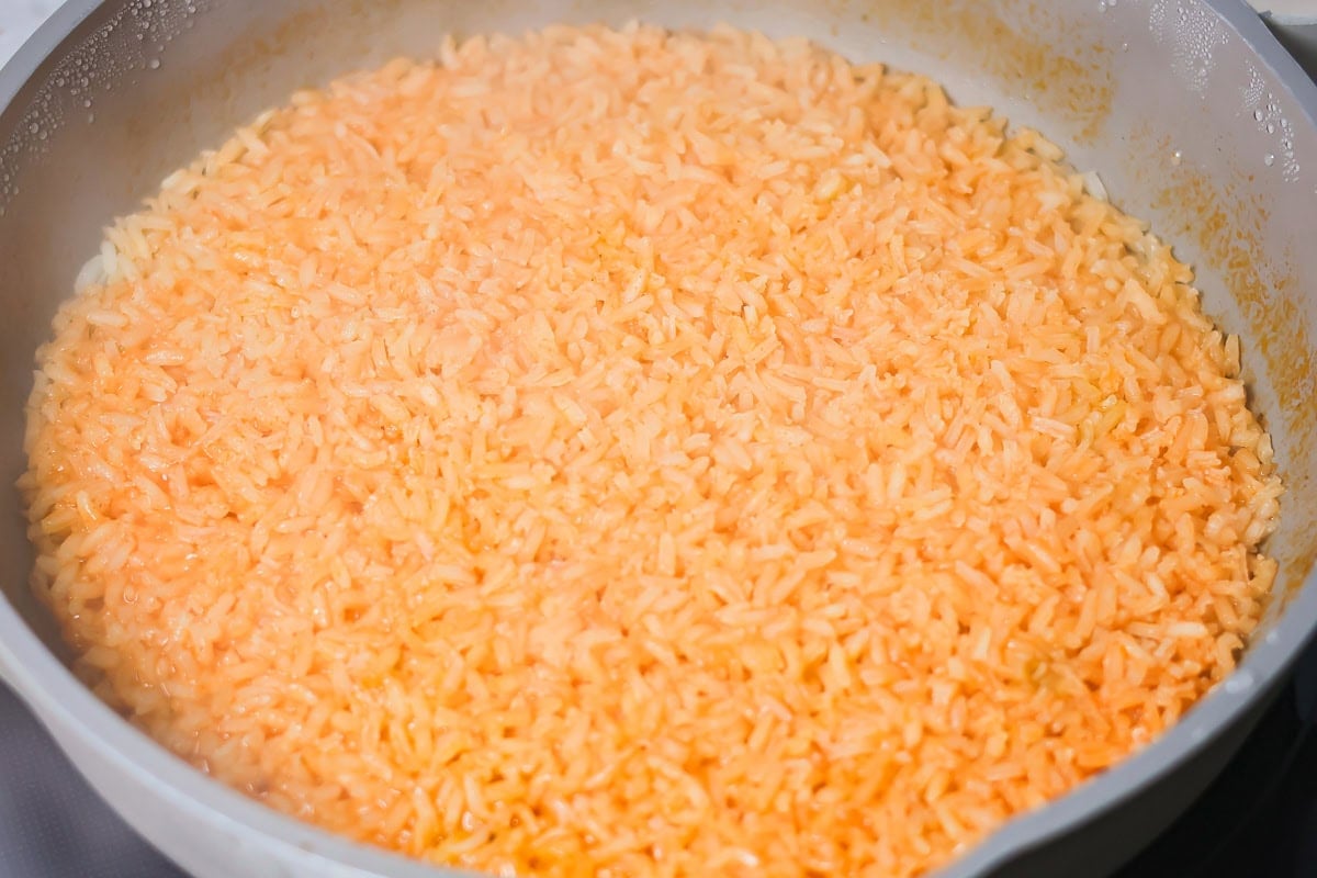 Grandma's famous caldo de pollo is a cozy chicken soup filled with chicken, rice, and Mexican spices and flavors! A pan of Spanish rice cooking in a pan.