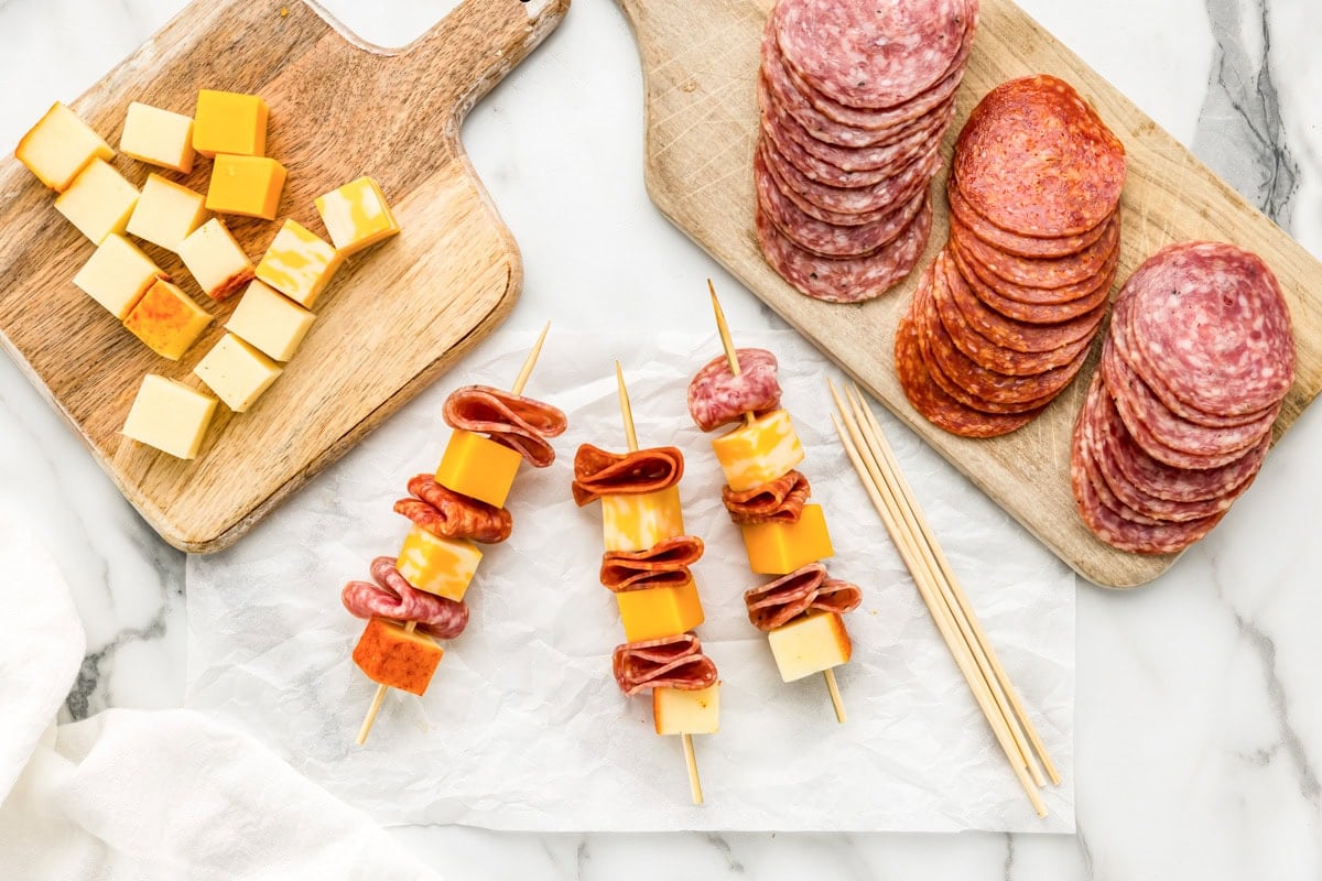 Assembling meats and cheeses on skewers.
