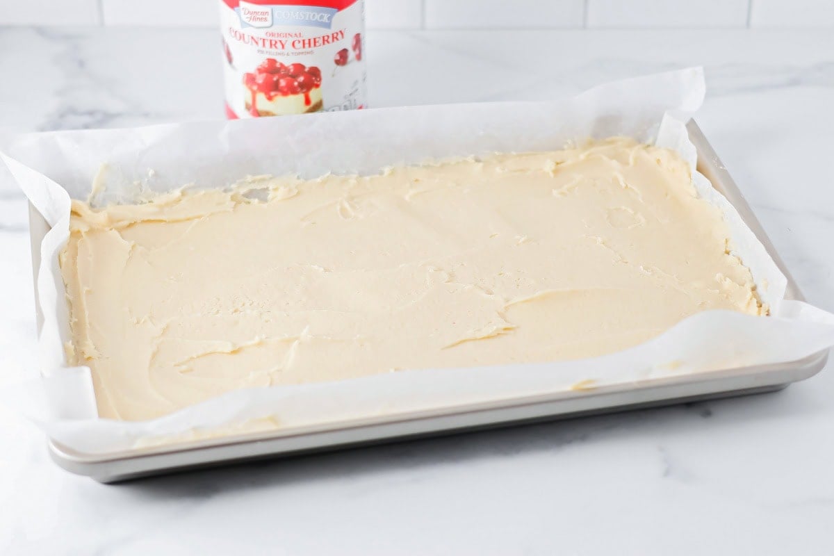 The base of cherry bars pressed into a parchment paper lined pan.
