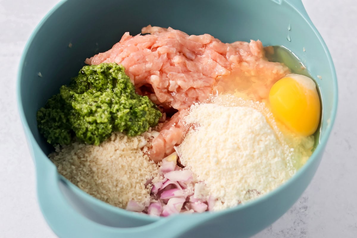 These easy chicken pesto meatballs come together in 30 minutes for a flavorful, family-friendly dinner full of basil and parmesan goodness. Unmixed meatball ingredients in a bowl.