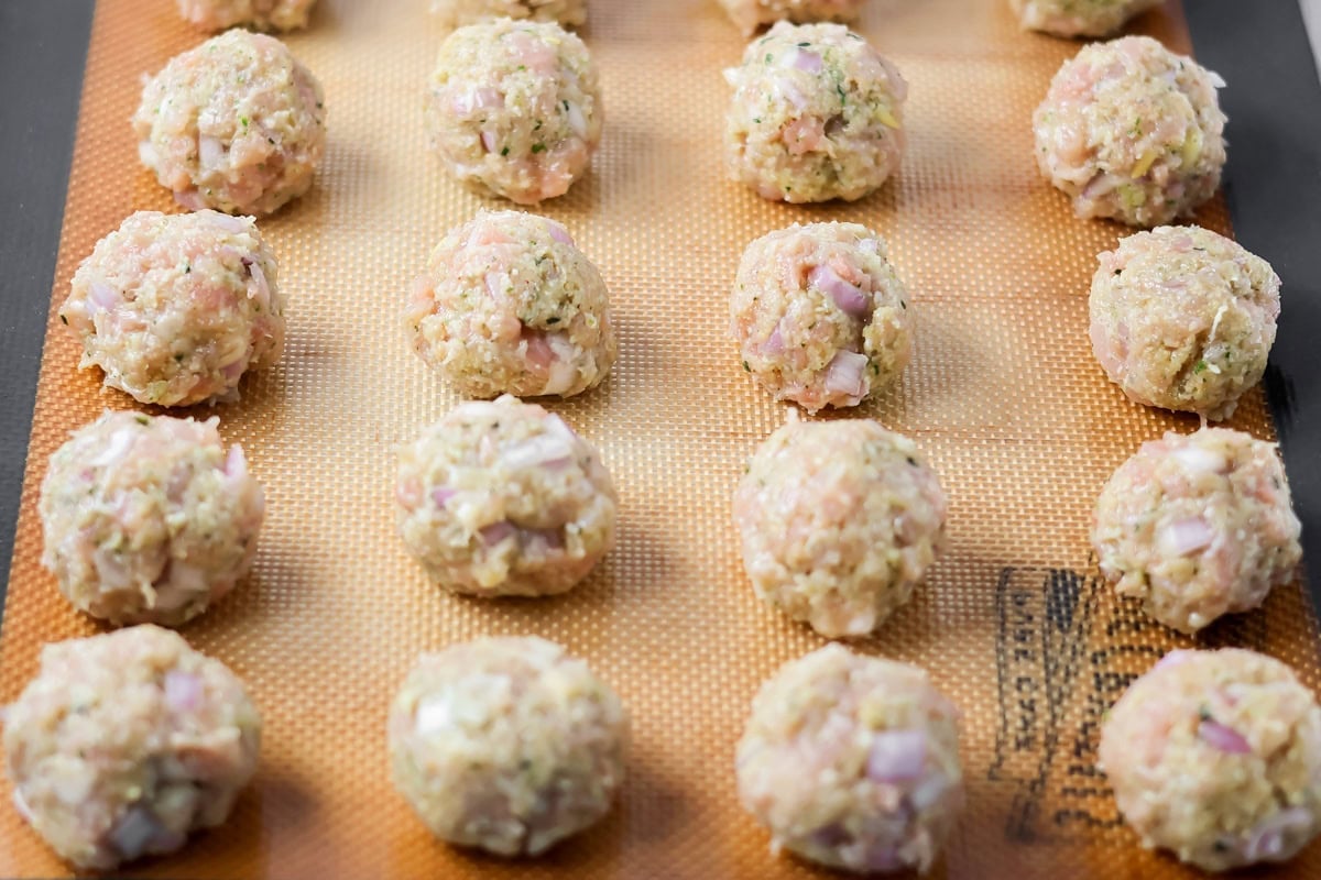 These easy chicken pesto meatballs come together in 30 minutes for a flavorful, family-friendly dinner full of basil and parmesan goodness. Raw meatballs on a baking sheet.