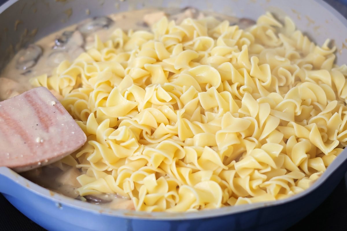 Creamy chicken stroganoff is perfect for dinner any night of the week. It's full of flavor and is made, start to finish, in about 30 minutes! Adding cooked egg noodles to the pan.