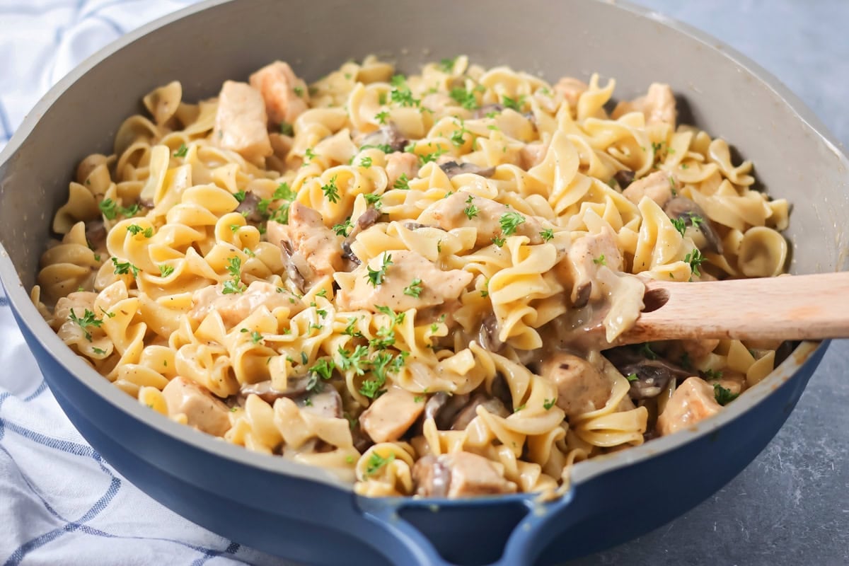 Creamy chicken stroganoff is perfect for dinner any night of the week. It's full of flavor and is made, start to finish, in about 30 minutes! Stirring noodles with creamy chicken and mushroom gravy.