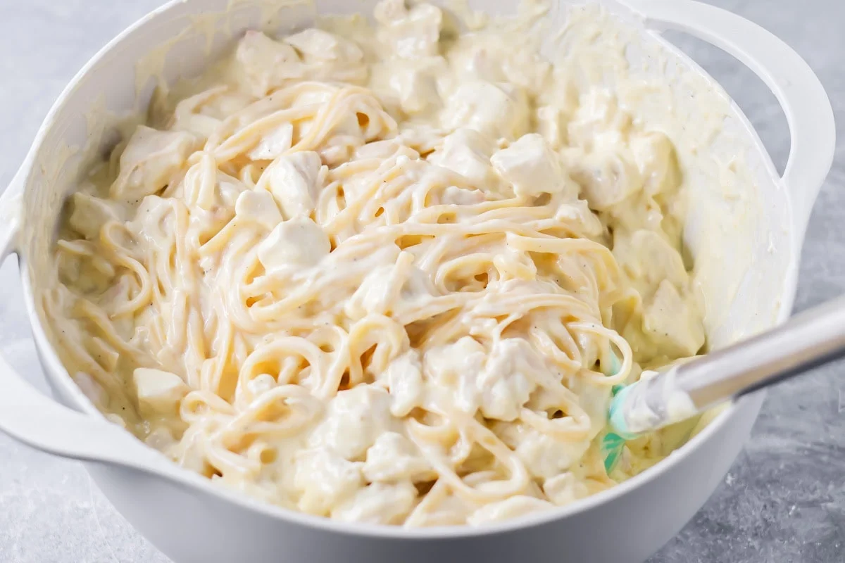 Mixing noodles into the tetrazzini sauce in a mixing bowl.