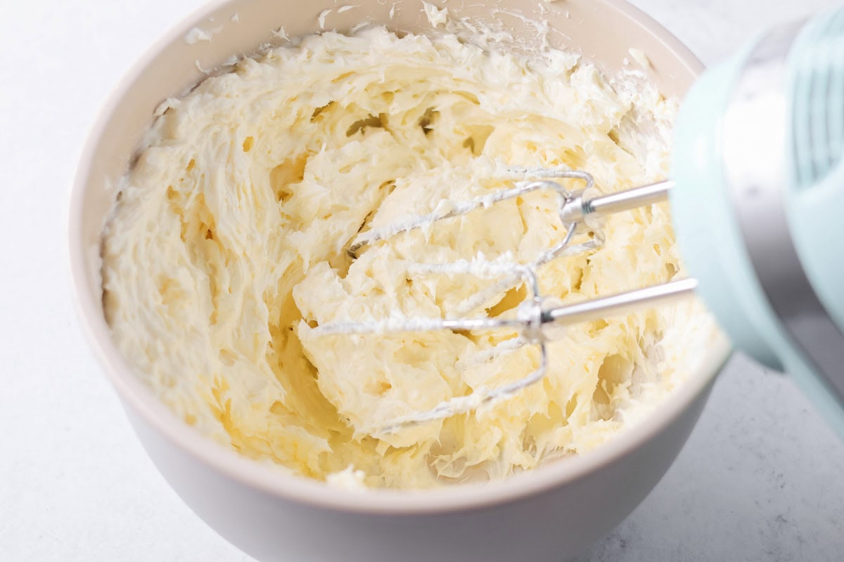 Mixing cream cheese and butter in a mixing bowl with an electric mixer.