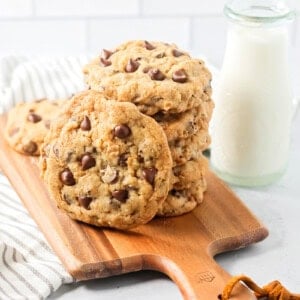 A stack of copycat Doubletree cookies on a cutting board served alongside milk.