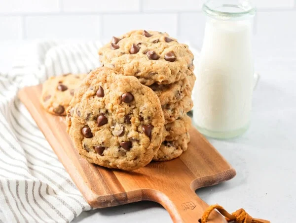 A stack of copycat Doubletree cookies on a cutting board served alongside milk.