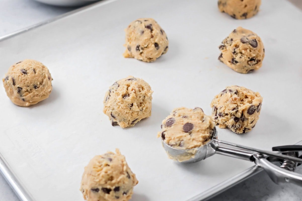 Copycat Doubletree cookies are big, chewy, and baked soft in the center with crisp edges for the ultimate treat. Scooping cookie dough onto a parchment lined baking sheet.