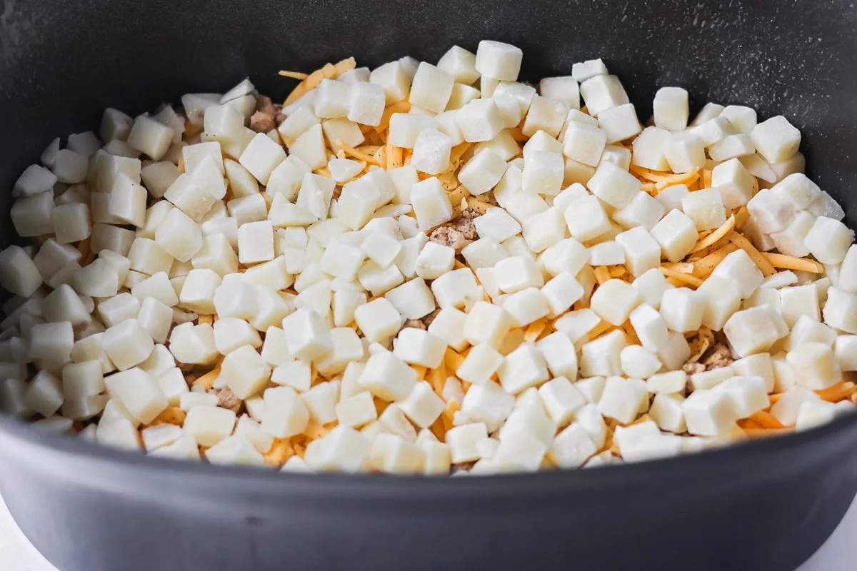 Crockpot breakfast casserole layers favorite breakfast foods for an easy and cozy dish that feeds a crowd with almost no effort. A layer of frozen hash browns on top of cheese and sausage in a crock pot.