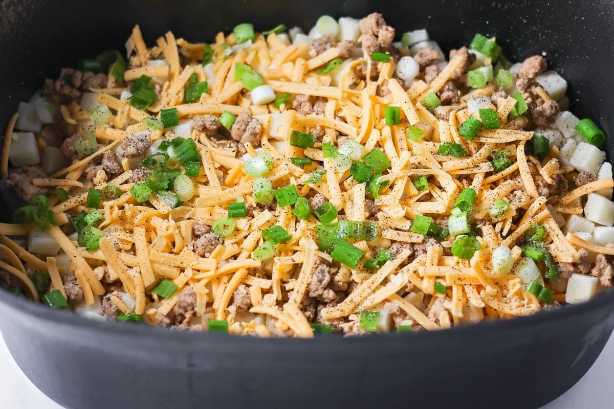 Crockpot breakfast casserole layers favorite breakfast foods for an easy and cozy dish that feeds a crowd with almost no effort. Final layer of shredded cheese and sausage added to a crock pot.