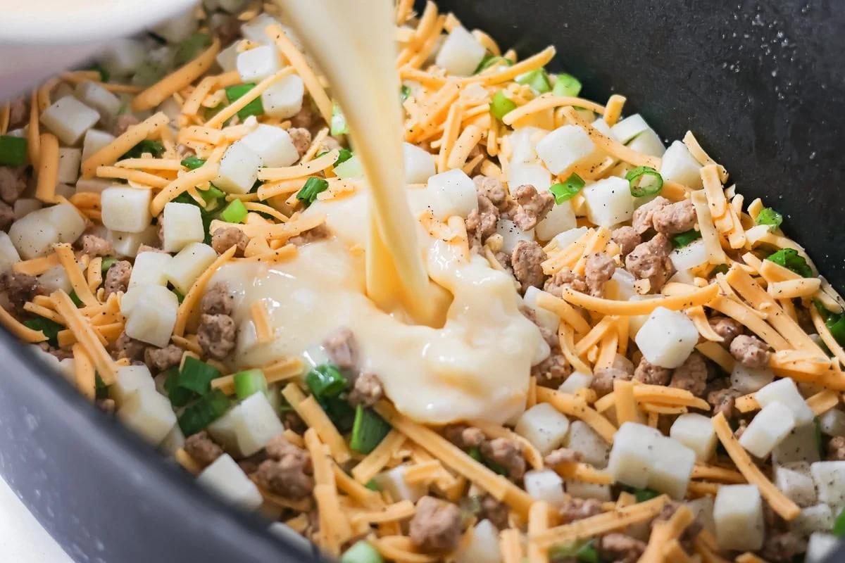 Crockpot breakfast casserole layers favorite breakfast foods for an easy and cozy dish that feeds a crowd with almost no effort. Pouring an egg custard mix over the layers in a crockpot.